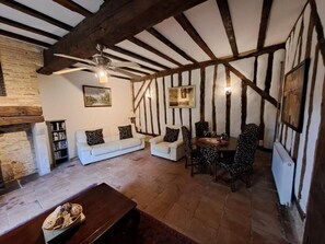 A traditional room with exposed wooden beams, a fireplace, a sofa set, a dining table with chairs, and a ceiling fan. - The four Oaks rural holiday (Le Fleix)