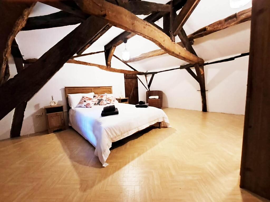 A bedroom with a wooden ceiling, a bed with a white bedspread, and a nightstand with a lamp.