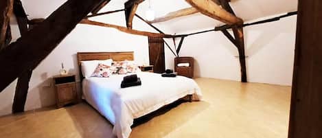 A bedroom with a wooden ceiling, a bed with a white bedspread, and a nightstand with a lamp.