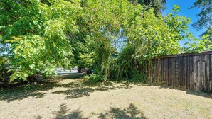 A backyard with a wooden fence, a grassy area, and trees. - Private Yard & Patio! Pet-Friendly Lynnwood Home (Lynnwood)