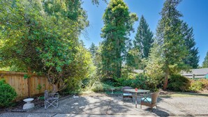 A backyard with a patio area, including a table and chairs, surrounded by dense foliage and tall trees. - Private Yard & Patio! Pet-Friendly Lynnwood Home (Lynnwood)
