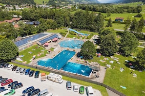 An aerial view of a resort with multiple swimming pools, a water slide, and a parking lot with various vehicles. - Holiday with Mountain Views in Mittersill (Mittersill)