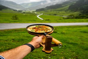 A hand holding a pan with a dish, set against a backdrop of a winding road through a green landscape. - Holiday with Mountain Views in Mittersill (Mittersill)