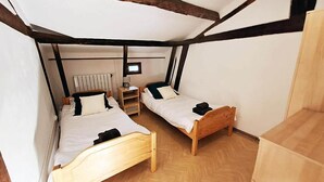 A small, cozy room with two wooden beds, a wooden wardrobe, a radiator, and a television. - Mulberry Lodge 16th Century farmhouse in rural setting (Le Fleix)