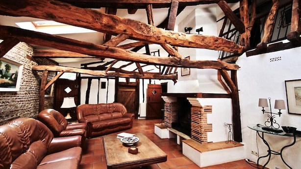 A rustic interior with exposed wooden beams, a leather sofa, a fireplace, and a table with a book. - Mulberry Lodge 16th Century farmhouse in rural setting (Le Fleix)