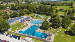 An aerial view of a resort with multiple swimming pools, a water slide, and a parking lot with various vehicles. - Stylish Apartment with Mountain Views (Mittersill)