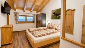 A bedroom with a wooden bed, a wardrobe, a television, a window with curtains, and a painting of a cow. - Stylish Apartment with Mountain Views (Mittersill)
