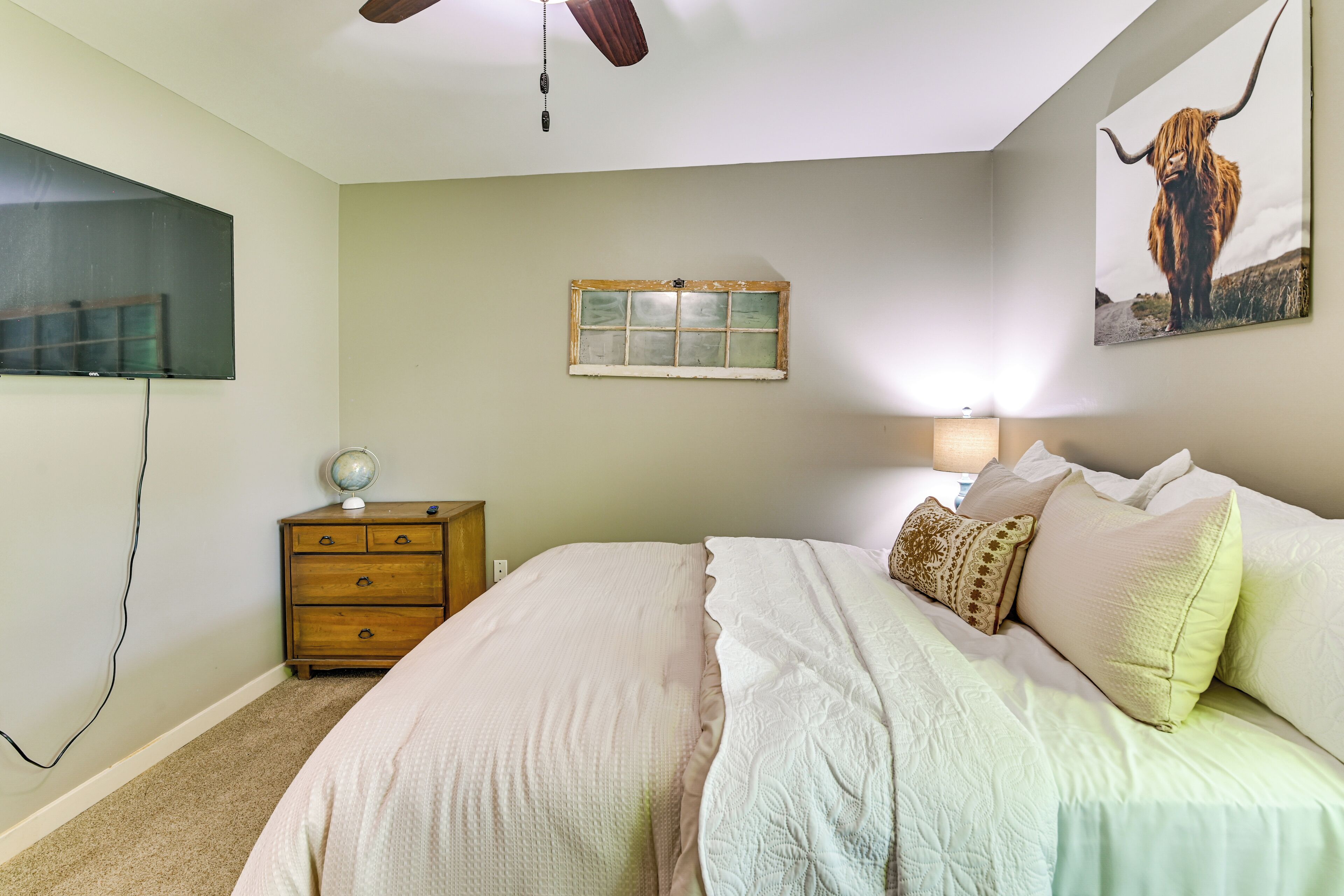 A bedroom with a bed, a dresser, a globe on the dresser, a window, and a wall-mounted picture.