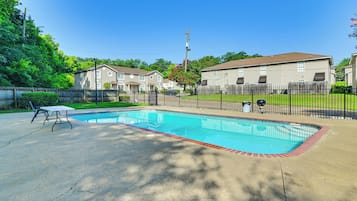Une piscine résidentielle entourée d’une clôture, avec une table de pique-nique et des maisons en arrière-plan.