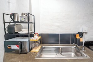 A kitchen with a stainless steel sink, a microwave, a toaster, and a shelf with utensils. - The 260 Collection Luxury City Apartment (Johannesburg)