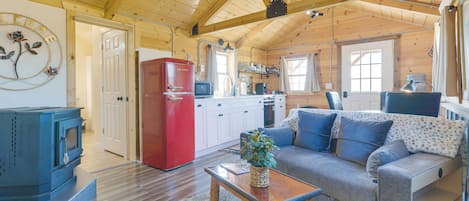 A cozy cabin interior with a wooden ceiling, a red refrigerator, a kitchenette, a sofa, and a blue television.
