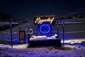 Ein verschneiter Außenbereich mit einem Neon-Schild, das 'Eggerhof' zeigt, und einer blauen, kreisförmigen Struktur.