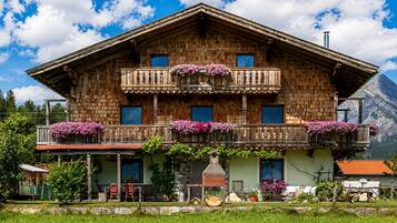 Eine zweistöckige Holzhütte mit Balkonen, die mit Blumen geschmückt sind, einer Veranda mit Sitzgelegenheiten und einem Berg im Hintergrund.
