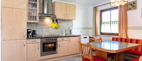 A compact kitchen with wooden cabinets, a built-in oven, and a dining area with a glass table and red cushioned chairs.
