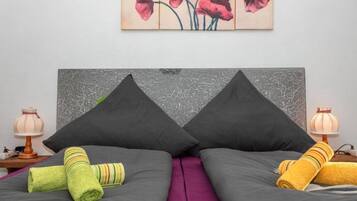 Een bed met twee kussens, een paarse dekbedovertrek en twee opgerolde handdoeken.