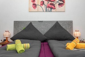 Un lit avec deux oreillers, une couvre-lit violette et deux serviettes enroulées.
