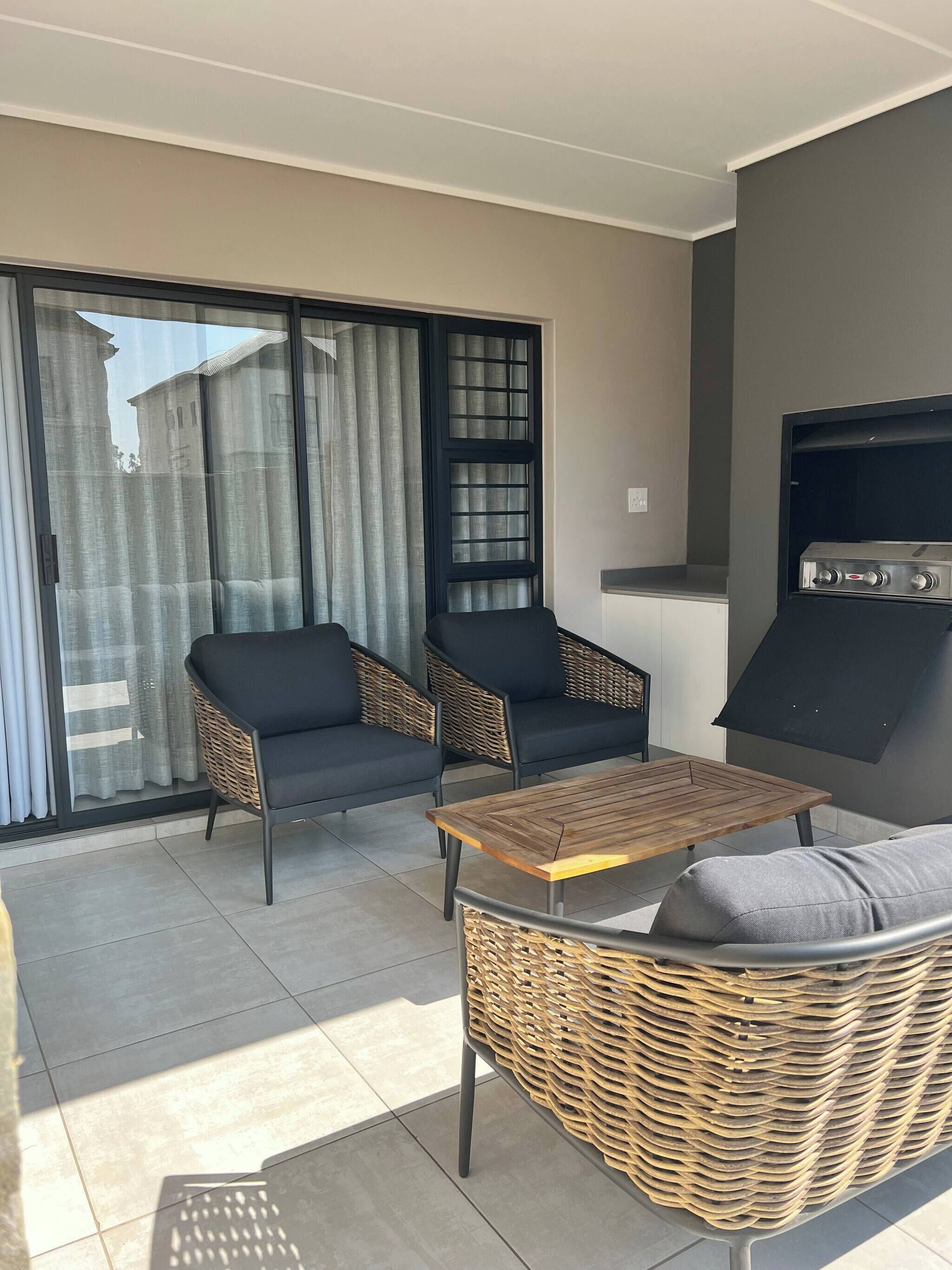 Ein Balkon mit zwei schwarzen Sofas, einem Holztisch und einem Grill.