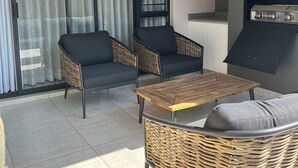 Un balcone con due divani neri, un tavolo di legno e un barbecue.