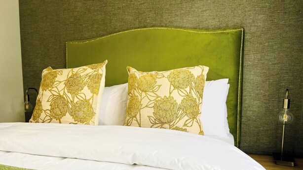 Un letto ben rifatto con biancheria bianca e tocchi di verde, una testiera imbottita verde e due cuscini decorativi con motivo floreale.
