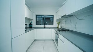 Una cucina moderna con mobili bianchi, un'isola centrale, una finestra sopra il lavello e una parete rivestita in marmo.