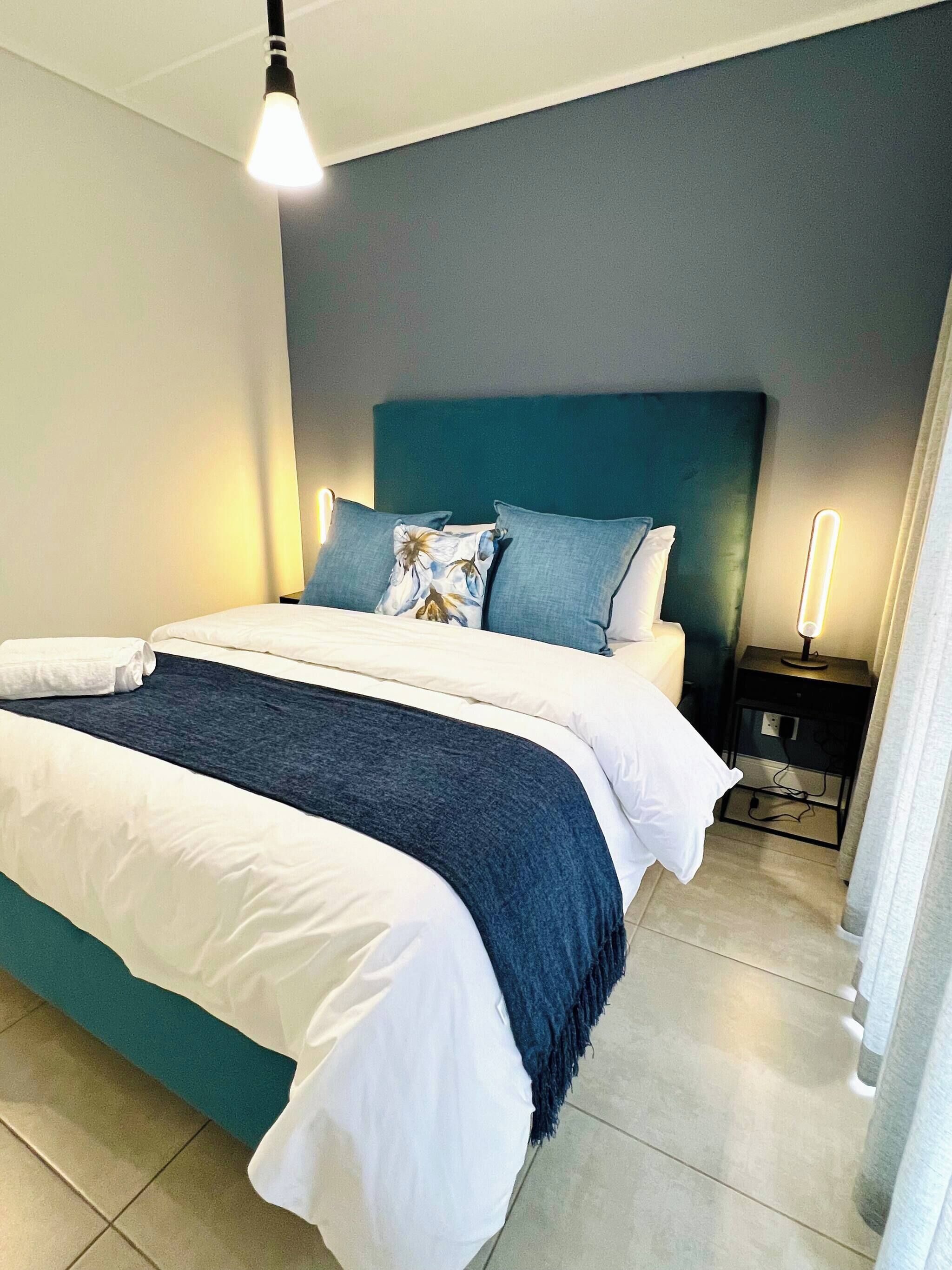 Un lit bien fait, avec une tête de lit bleue, du linge de lit blanc et un plaid bleu.