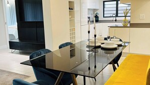 Un'area pranzo moderna con un tavolo in vetro, sedie blu e una panca gialla.