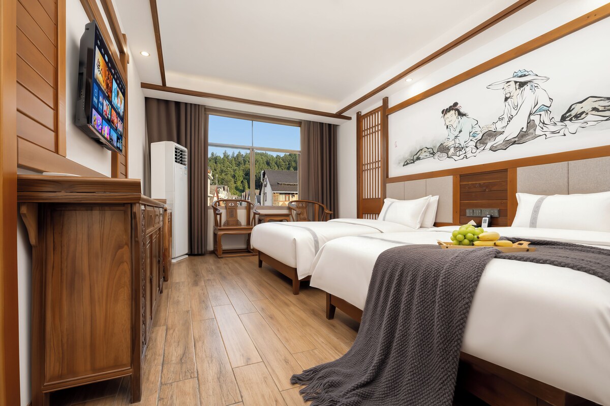 Quarto de hotel com duas camas, televisão, quadro e vista para uma floresta.