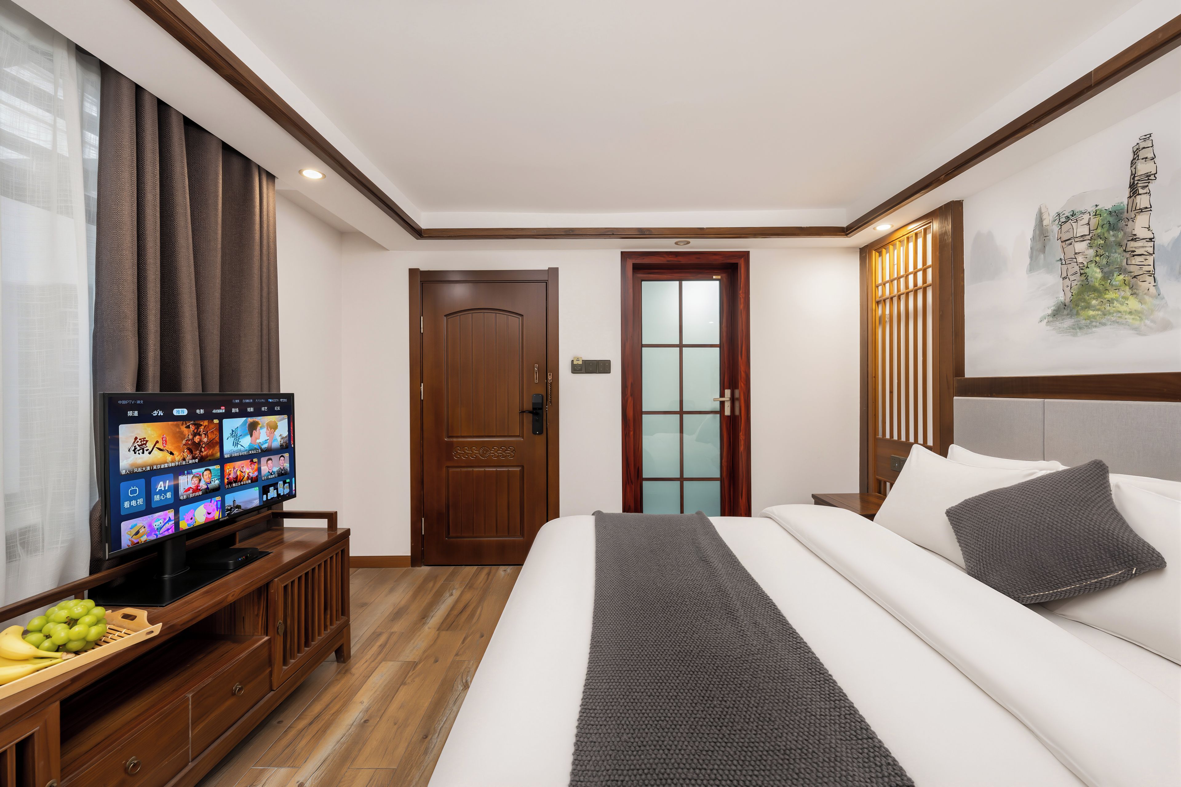 Une chambre d’hôtel avec un lit, un téléviseur posé sur un meuble en bois, une porte et un mur orné d’un panneau décoratif.