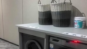 A laundry area with two washing machines, a basket, and a detergent container. - HuaHarmony Wulingyuan City Inn (Zhangjiajie)