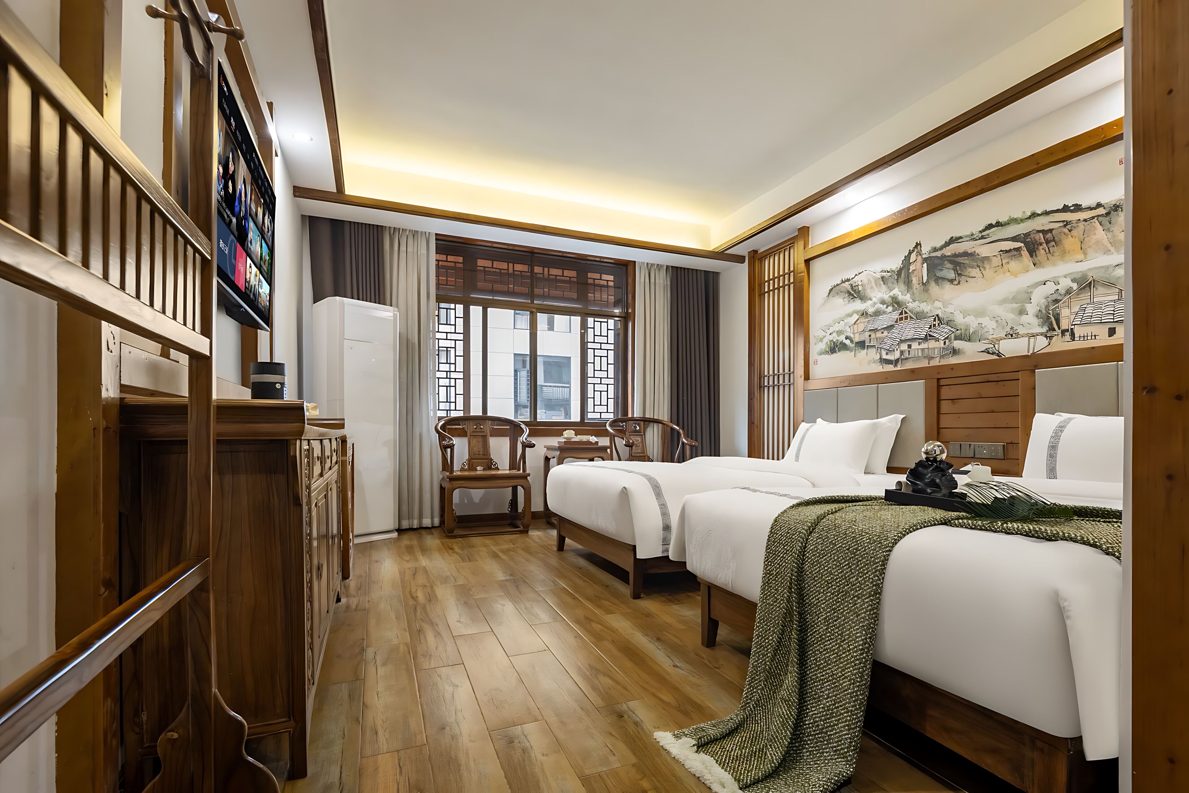 Une chambre d’hôtel avec un plancher en bois, un lit recouvert d’une couverture verte, un bureau avec une chaise, un téléviseur fixé au mur et un tableau accroché au mur.