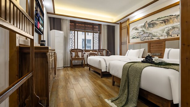 A hotel room with a wooden floor, a bed with a green blanket, a desk with a chair, a TV mounted on the wall, and a painting on the wall. - HuaHarmony Wulingyuan City Inn (Zhangjiajie)