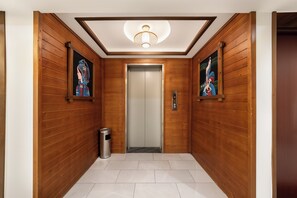 Un corridoio con rivestimenti in legno, pavimento piastrellato, un lampadario a soffitto e due opere d'arte incorniciate alle pareti.