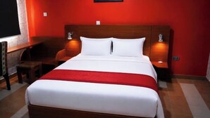 Une chambre d’hôtel avec un grand lit, une tête de lit en bois, deux tables de chevet avec des lampes et un mur d’accent rouge.