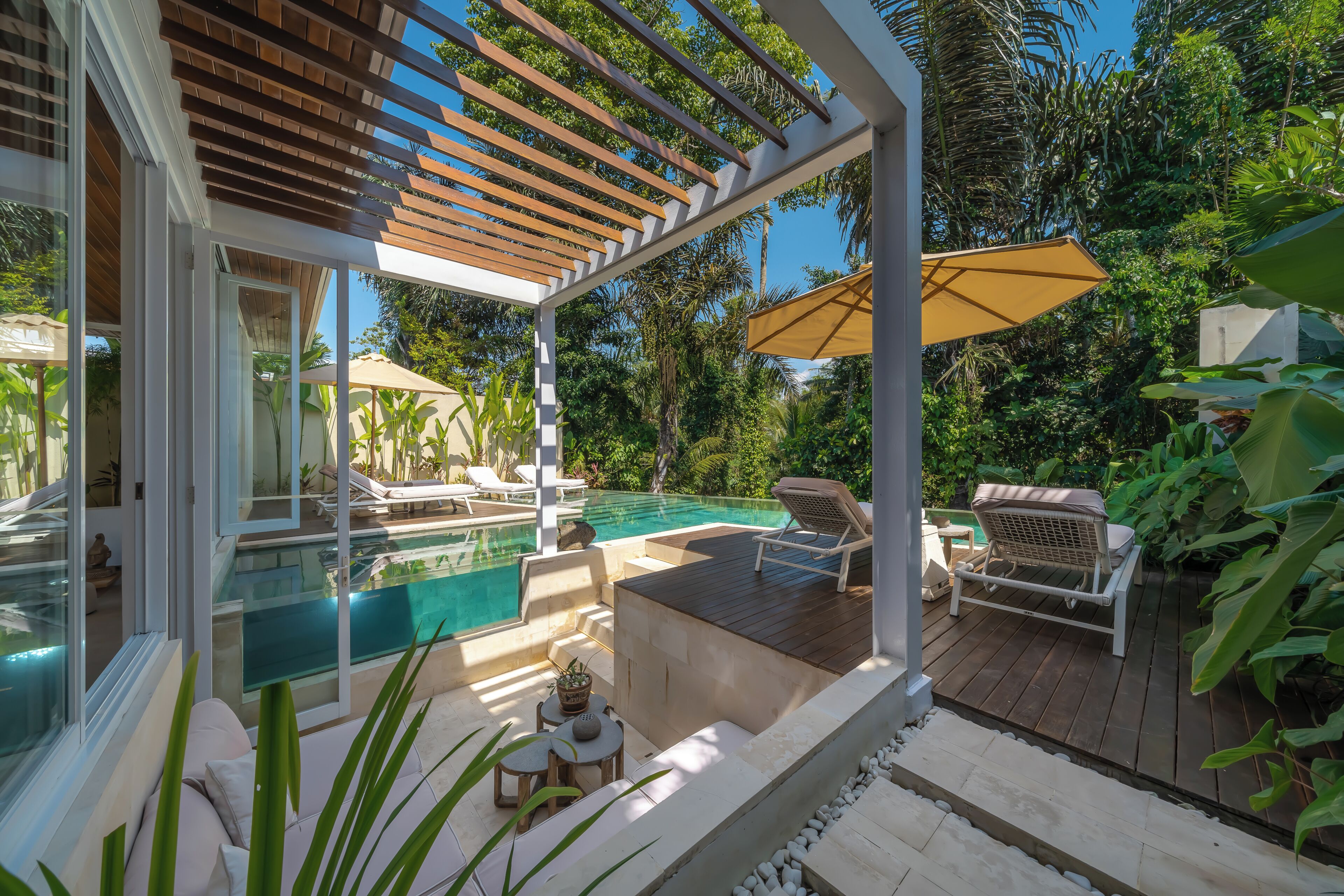 Zona de piscina con pérgola, sillas de descanso y una mesa con frutero.