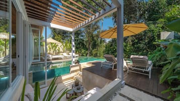 Zona de piscina con pérgola, sillas de descanso y una mesa con frutero.