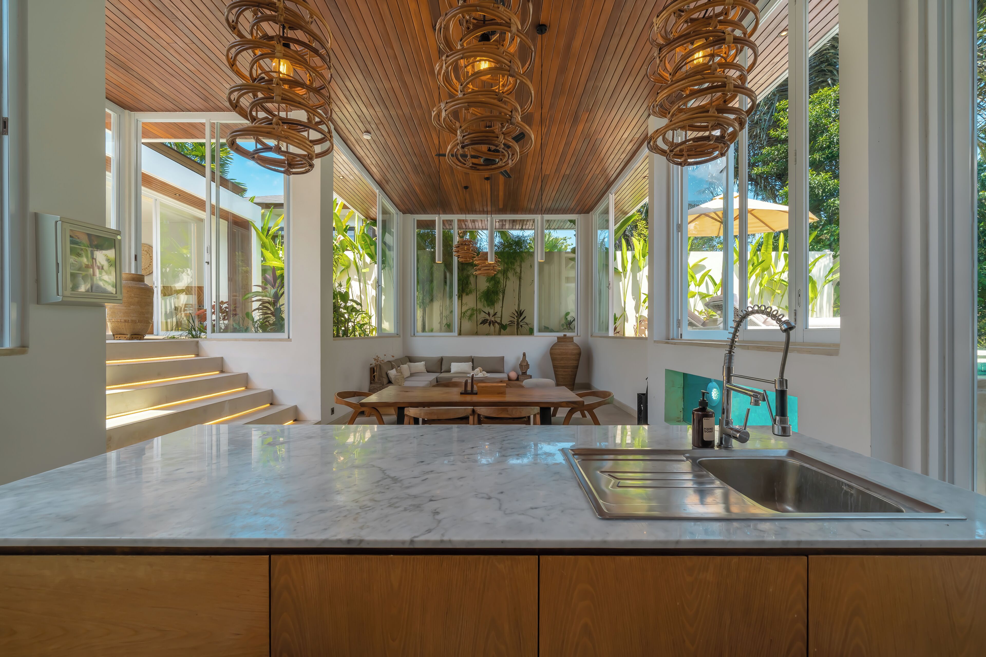 Una cocina moderna con encimera de mármol, un lavamanos integrado y una zona de comedor con mesa y sillas de madera.