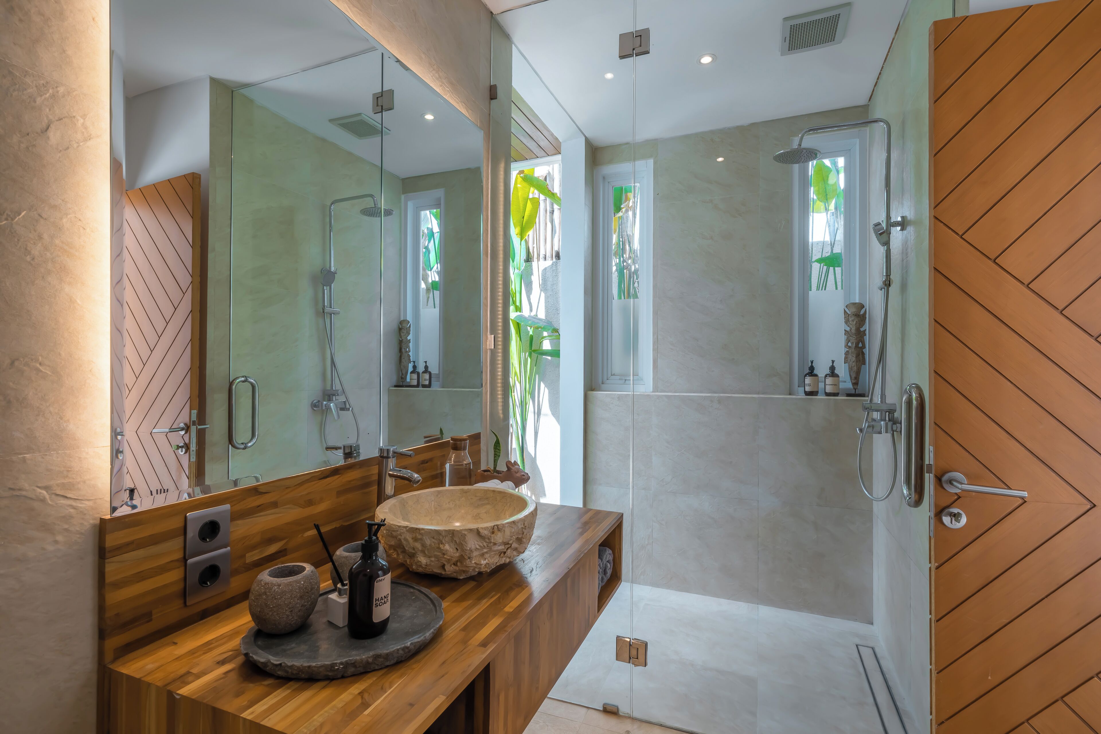 Un baño moderno con tocador de madera, un espejo grande, un lavabo de piedra y ducha con mampara de vidrio.