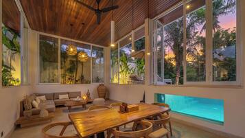 Un interior moderno con techo de madera, ventanas amplias, piscina y comedor.