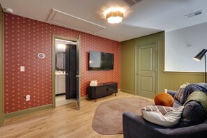 Ein Zimmer mit Holzboden, einer Couch, einem an der Wand montierten Fernseher und einer Tür zu einem Badezimmer.
