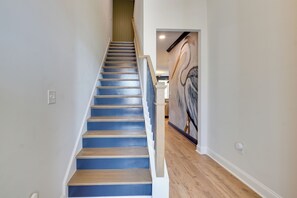 Eine Treppe mit HolzsStufen und blauen Wangen, die zu einem Raum mit einem großen, abstrakten Gemälde an der Wand führt.