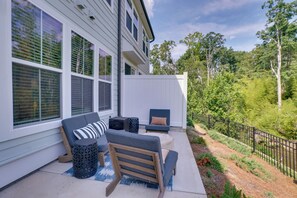 Eine Terrasse mit Gartenmöbeln, darunter eine Couch und Stühle, neben einem Haus mit großen Fenstern und einem weißen Zaun.
