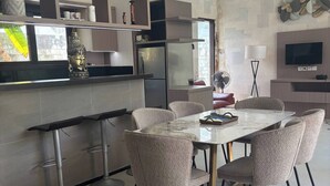 Et moderne køkken med et indbygget køleskab, et spiseområde med et marmorbord og polstrede stole, samt et vægmonteret fladskærms-tv.
