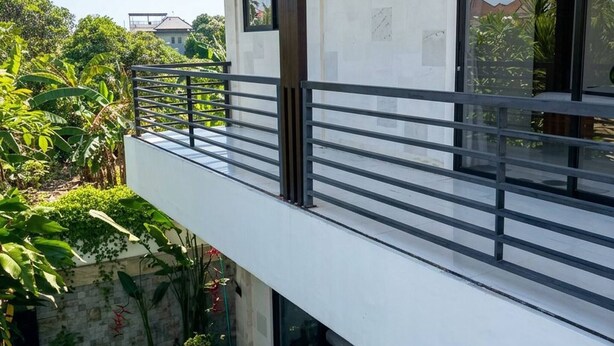 En moderne bygning i to etager med balkon, swimmingpool og frodig beplantning.