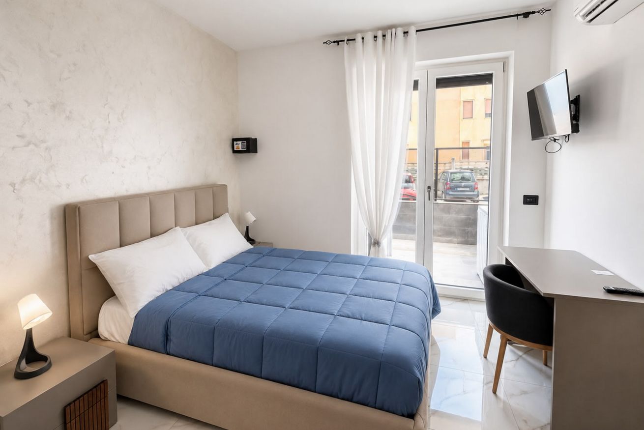 Ein Schlafzimmer mit Bett, Schreibtisch, Stuhl, Fernseher und einem Fenster mit Vorhängen.