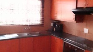 A kitchen with red cabinets, a black countertop, and a window with blinds. - Ametis Crescent Apartment (Middelburg)