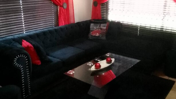 A living room with a dark blue sofa, a glass coffee table with red and white decorative items, and red curtains on the windows. - Ametis Crescent Apartment (Middelburg)