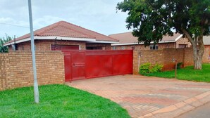 A residential property with a paved driveway, a red gate, and a brick wall. - Ametis Crescent Apartment (Middelburg)