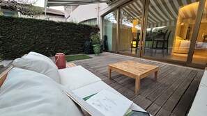 Une terrasse en bois avec un canapé blanc, une petite table et un vase rouge.