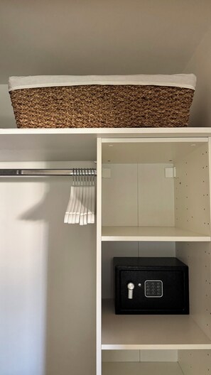 A storage closet with a woven basket on top, a metal rod with hanging items, and a black safe. - Stylish Garden Apartment ° Pool, Tennis & Parking ° Near Cannes (Mandelieu-la-Napoule)