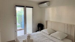 A bedroom with a bed, a window, and an air conditioning unit. - Stylish Garden Apartment ° Pool, Tennis & Parking ° Near Cannes (Mandelieu-la-Napoule)